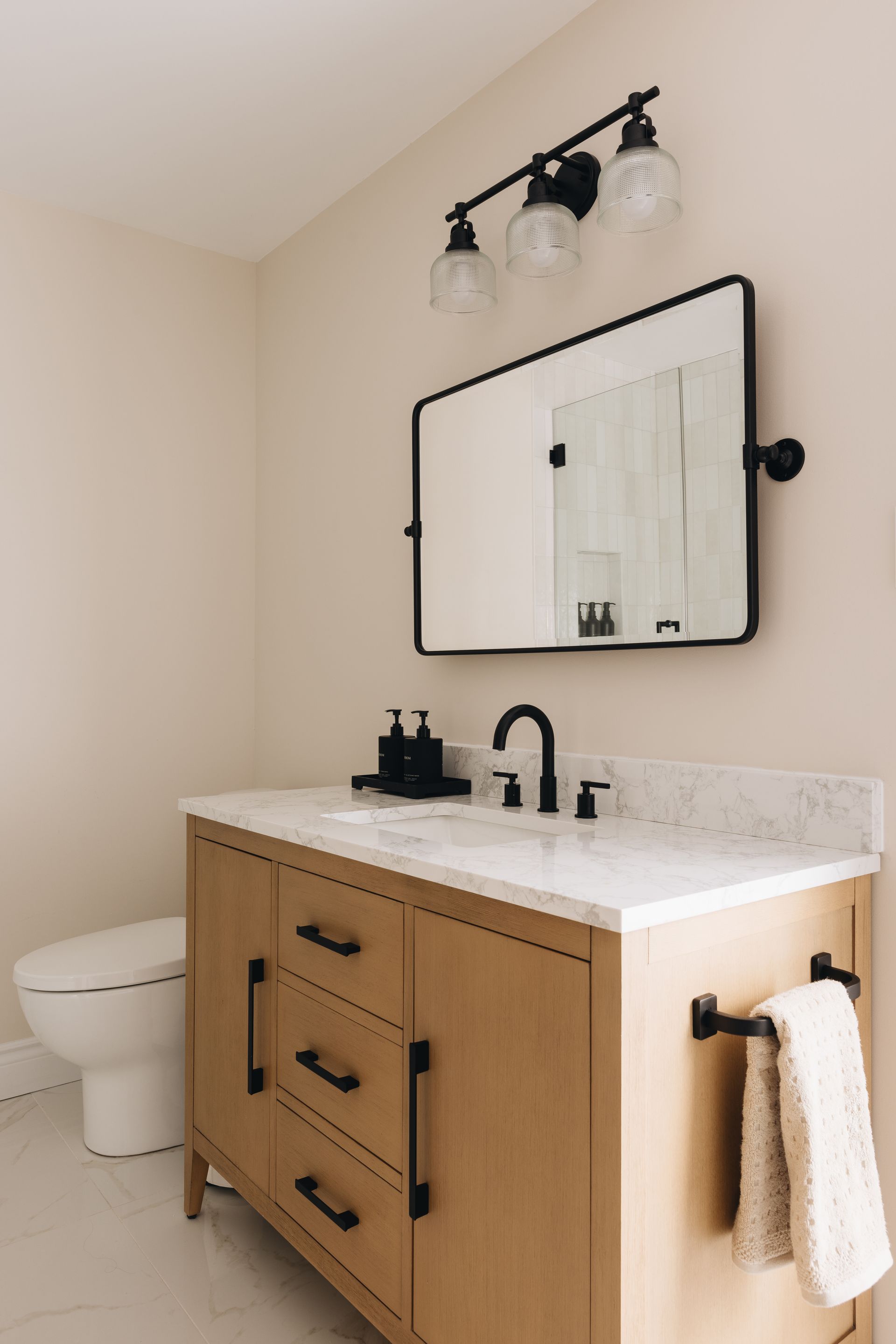 Bathroom with wooden vanity, black fixtures, and a rectangular mirror.
