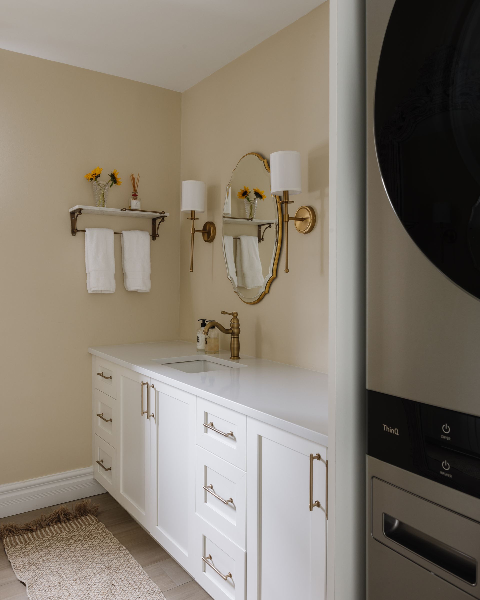 Bathroom with white vanity, gold fixtures, oval mirror, and washing machine visible.