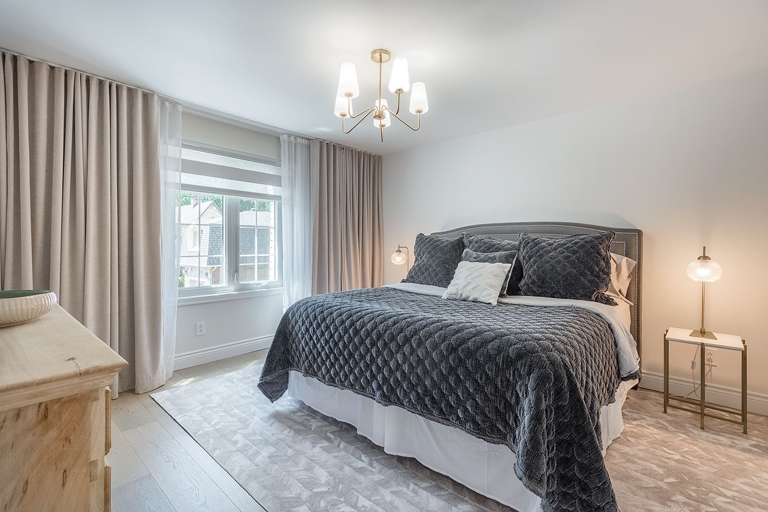 Bedroom with grey bedding, light curtains, and a chandelier.