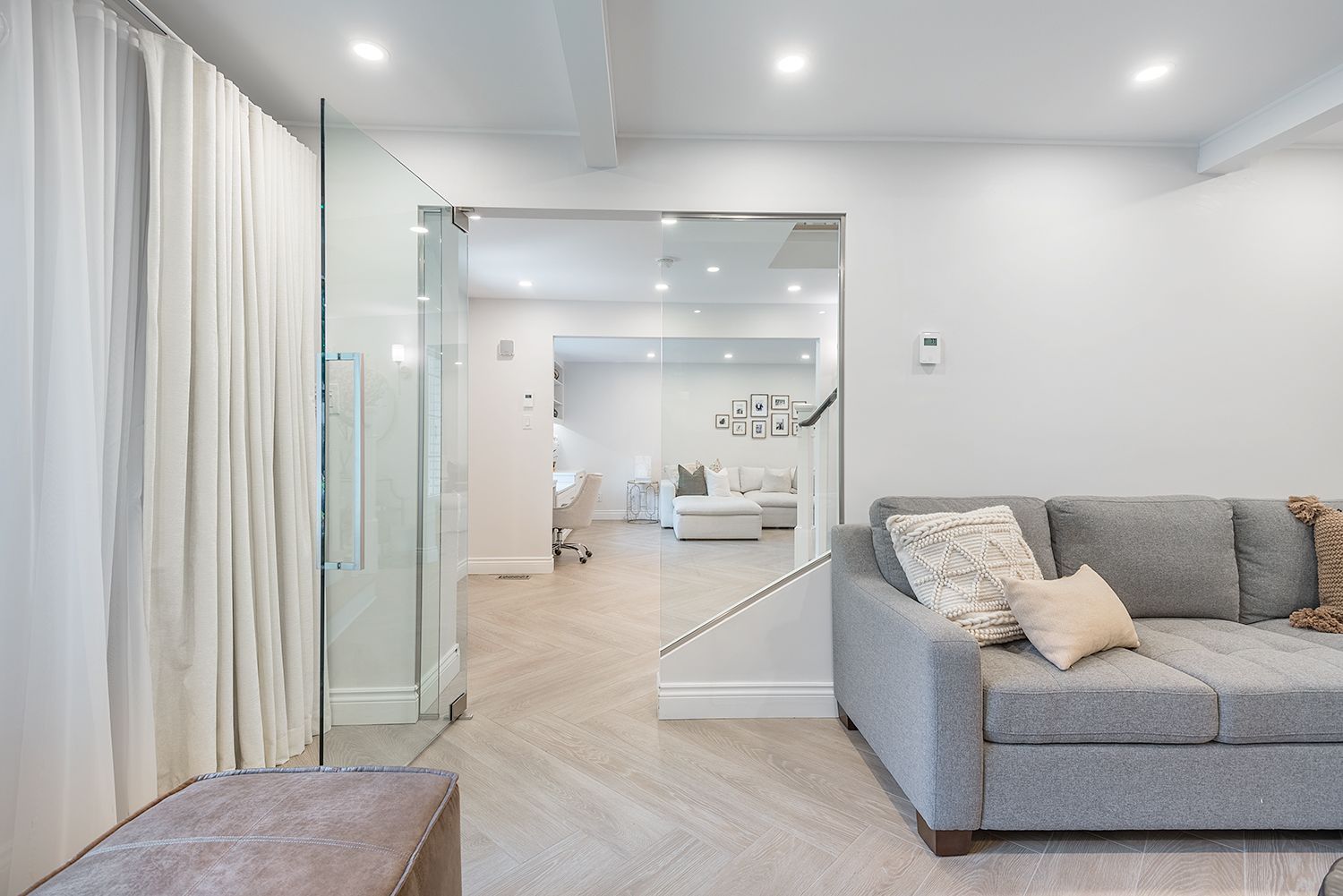 Living room with gray sofa, glass doorway, white curtains, and light-colored floor.