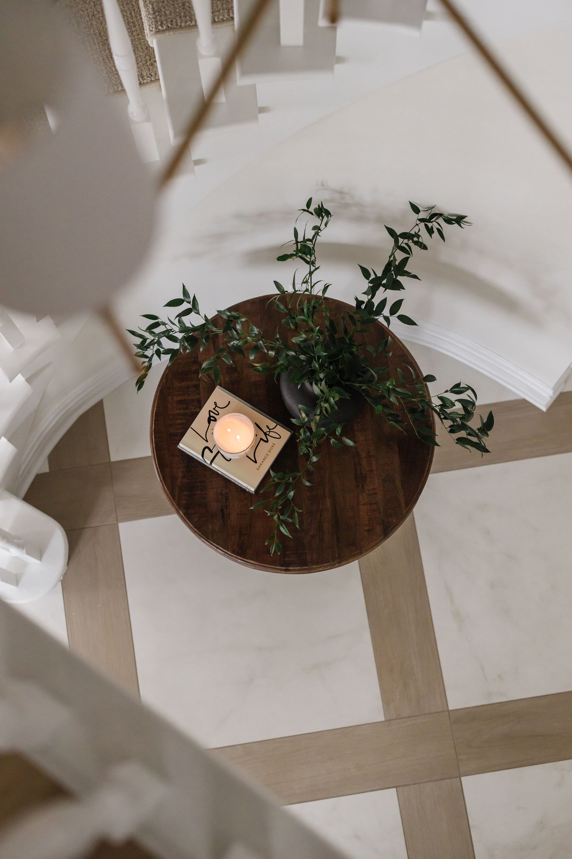 Overhead shot of a round, dark wooden table with greenery, a book, and a candle in a light-colored room.
