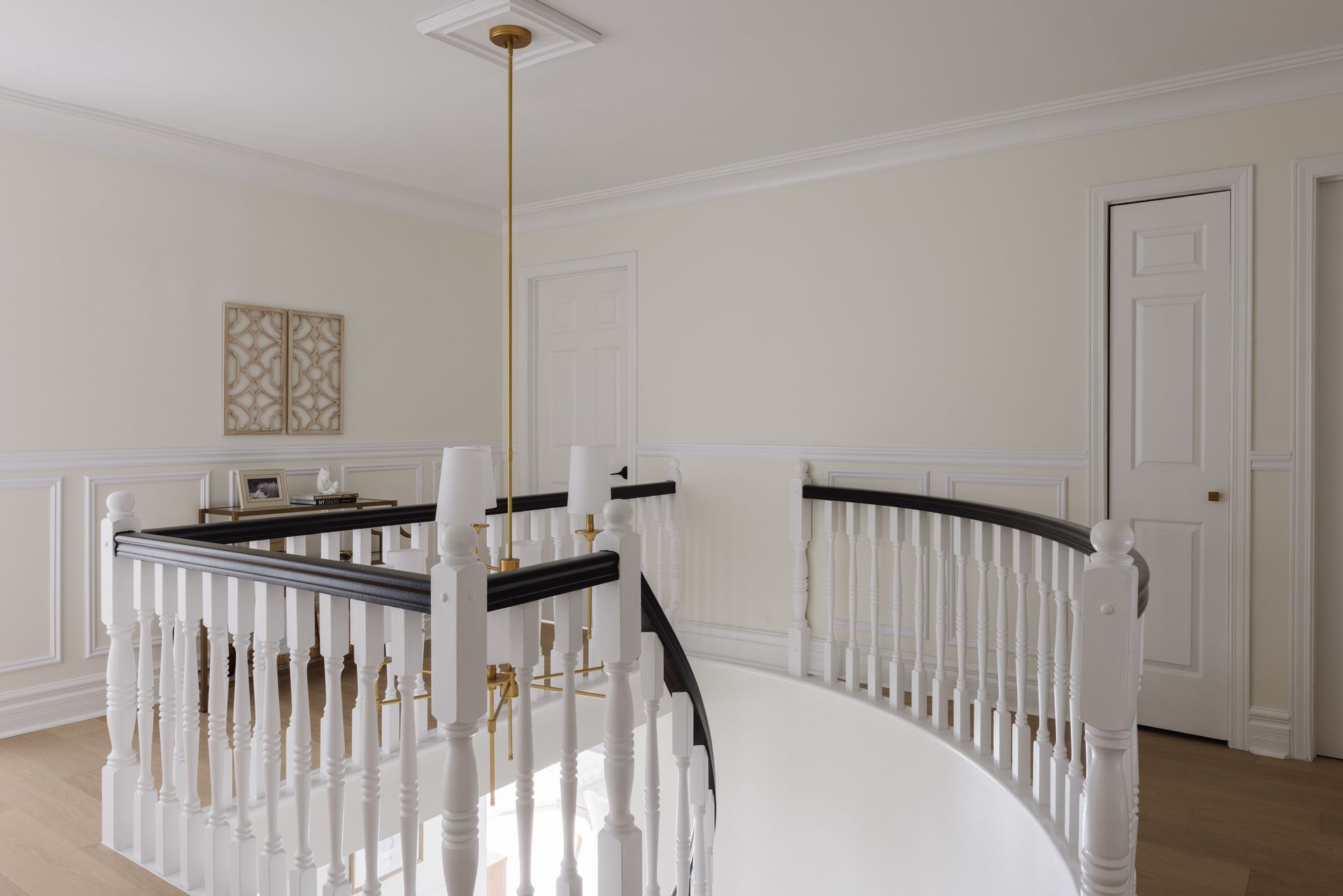 White and black banistered staircase with chandelier, leading to a hallway with white walls and a closed door.