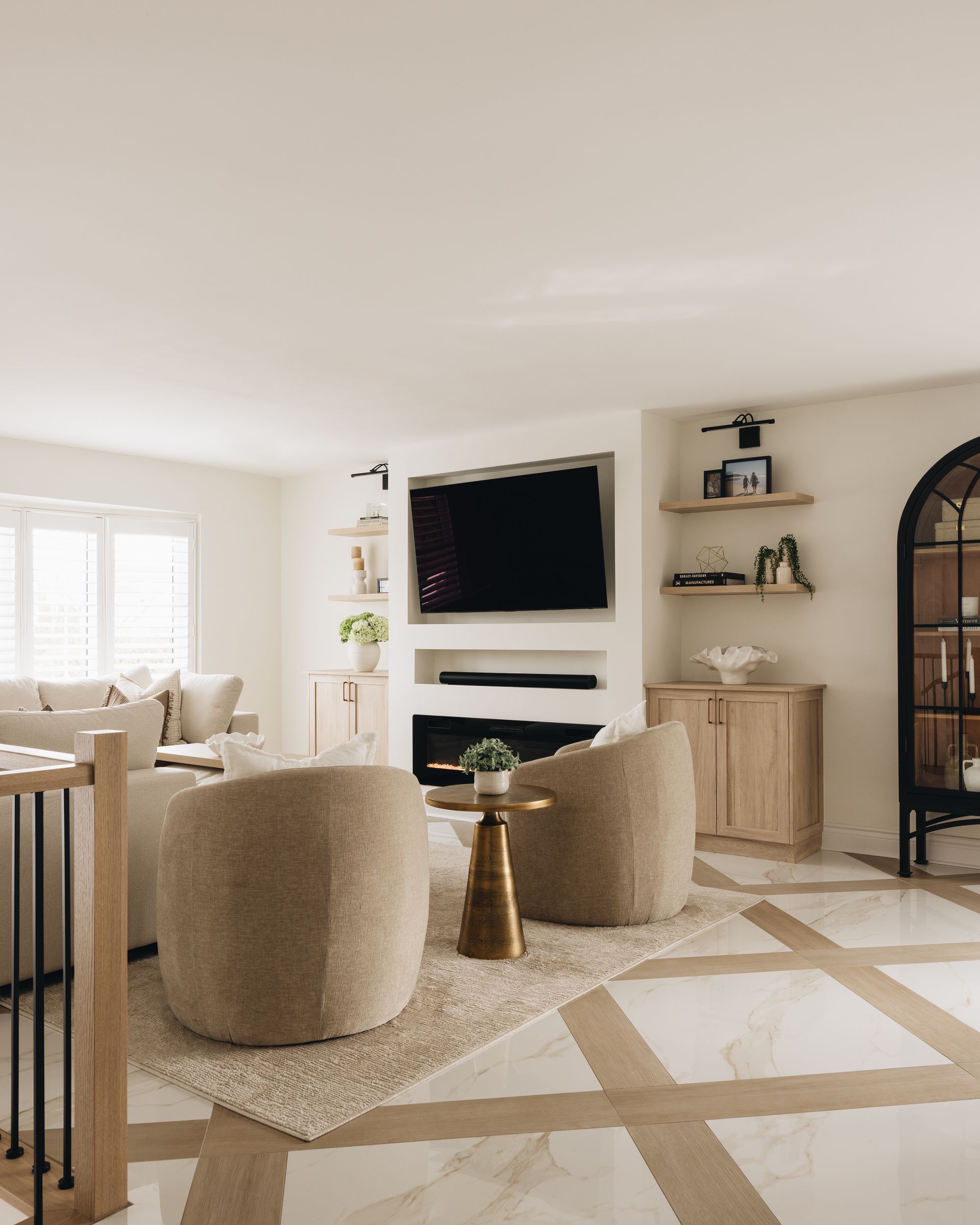 Living room with beige chairs, TV above fireplace, and light wood floors.