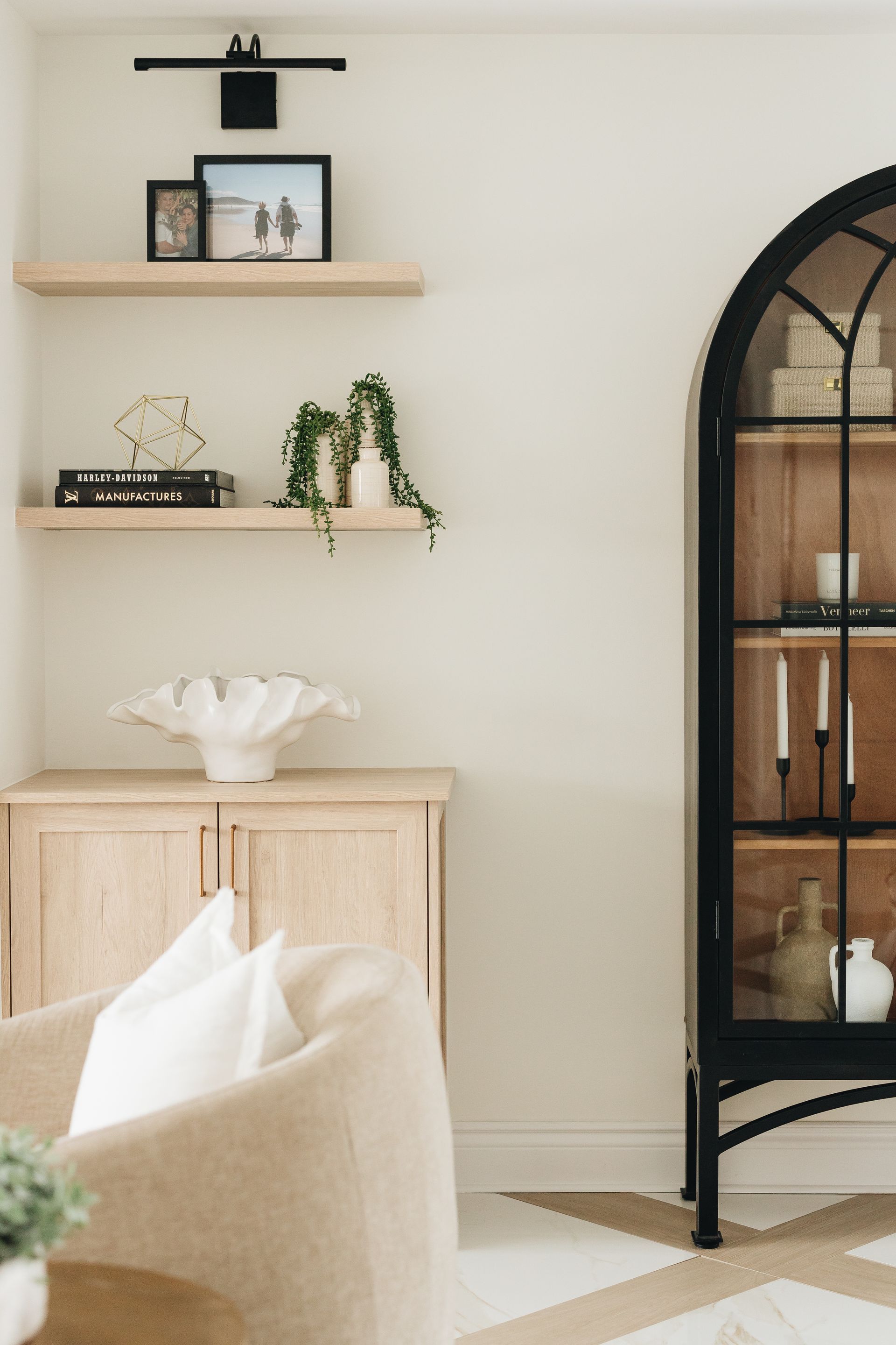 Living room with neutral tones, shelves with decor, arched cabinet, and beige chair.