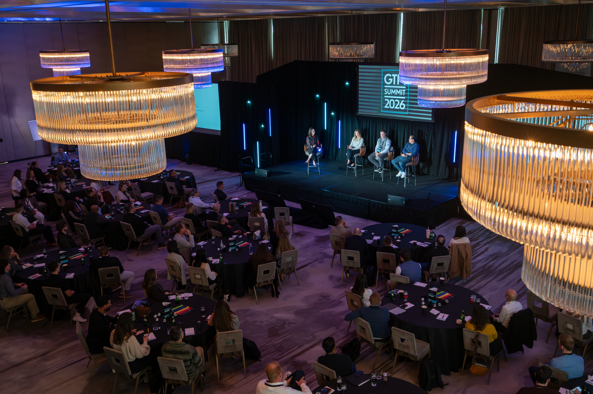 Wide-angle photograph capturing a corporate leadership panel and engaged conference attendees during a general session.
