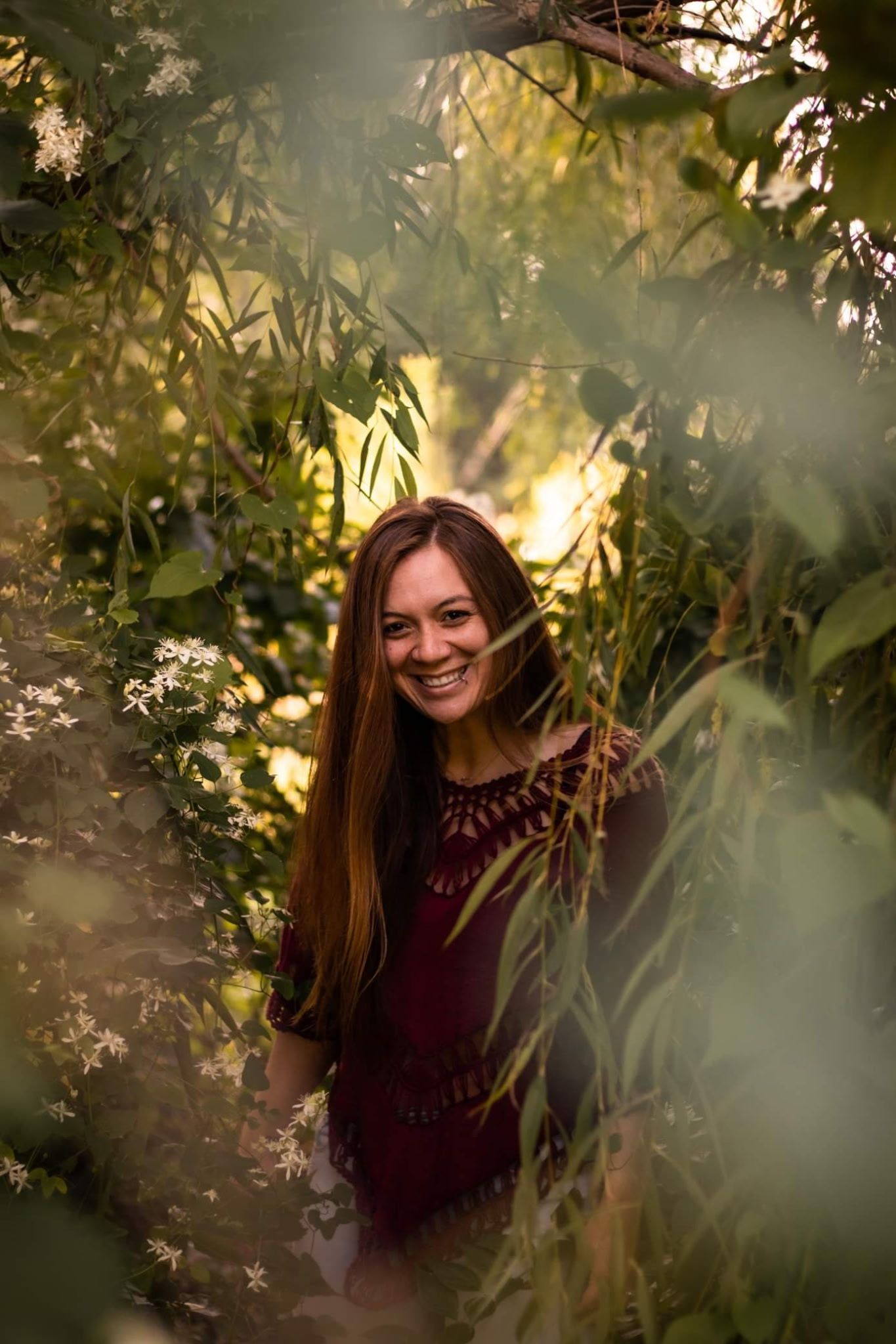 A woman is smiling while standing in the woods.