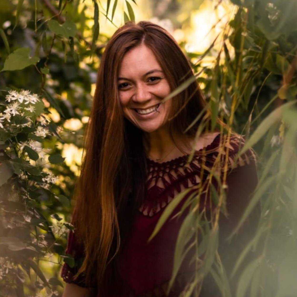 A woman is smiling while standing in the woods.