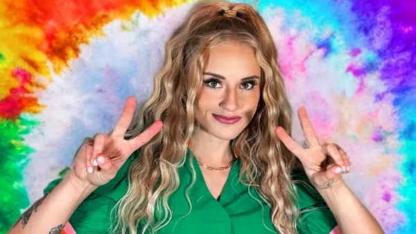 Woman with blonde wavy hair makes peace signs in front of a tie-dye background.
