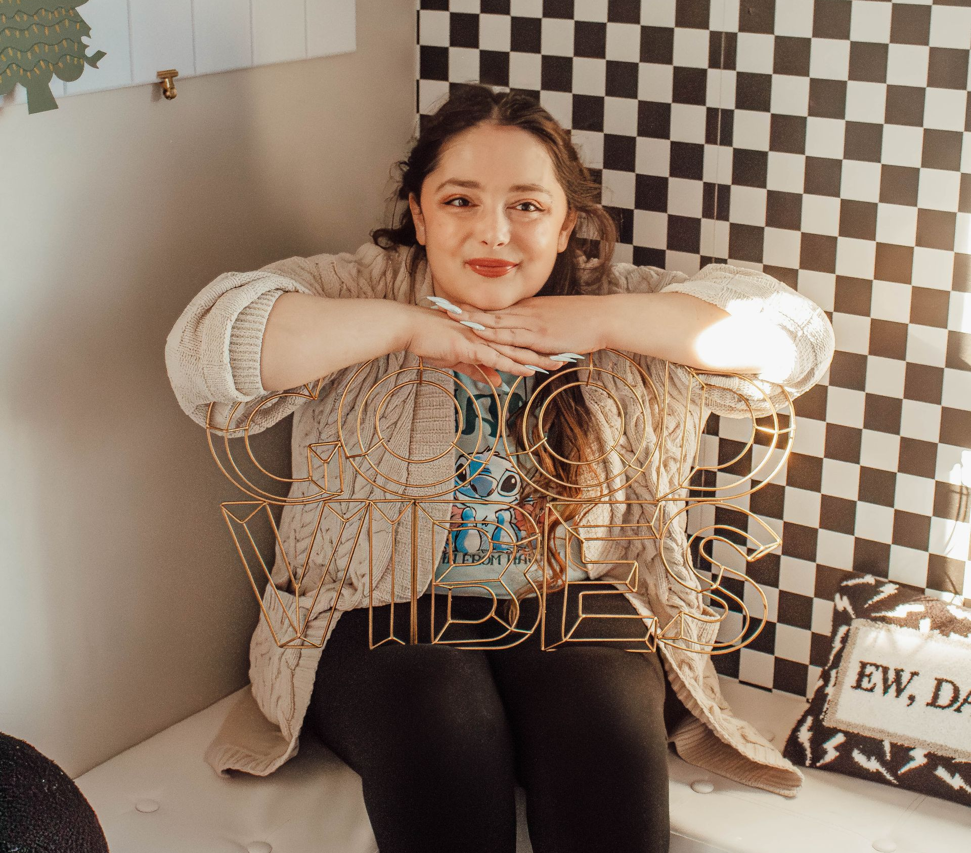 Person sitting on a chair with arms folded, in a cozy room with a black-and-white checkered wall.