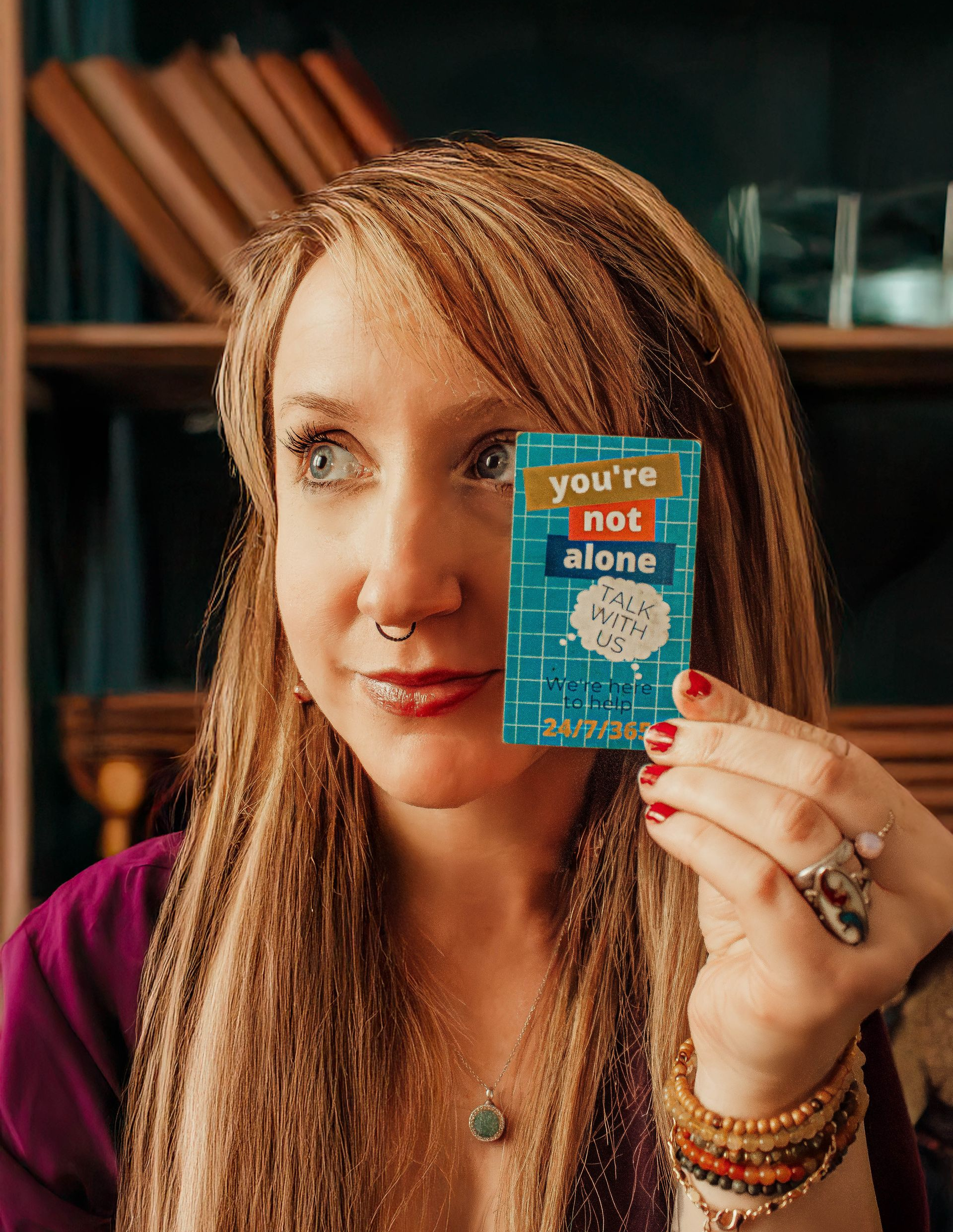 Woman holding up a small blue-orange card with text, seated indoors in warm light