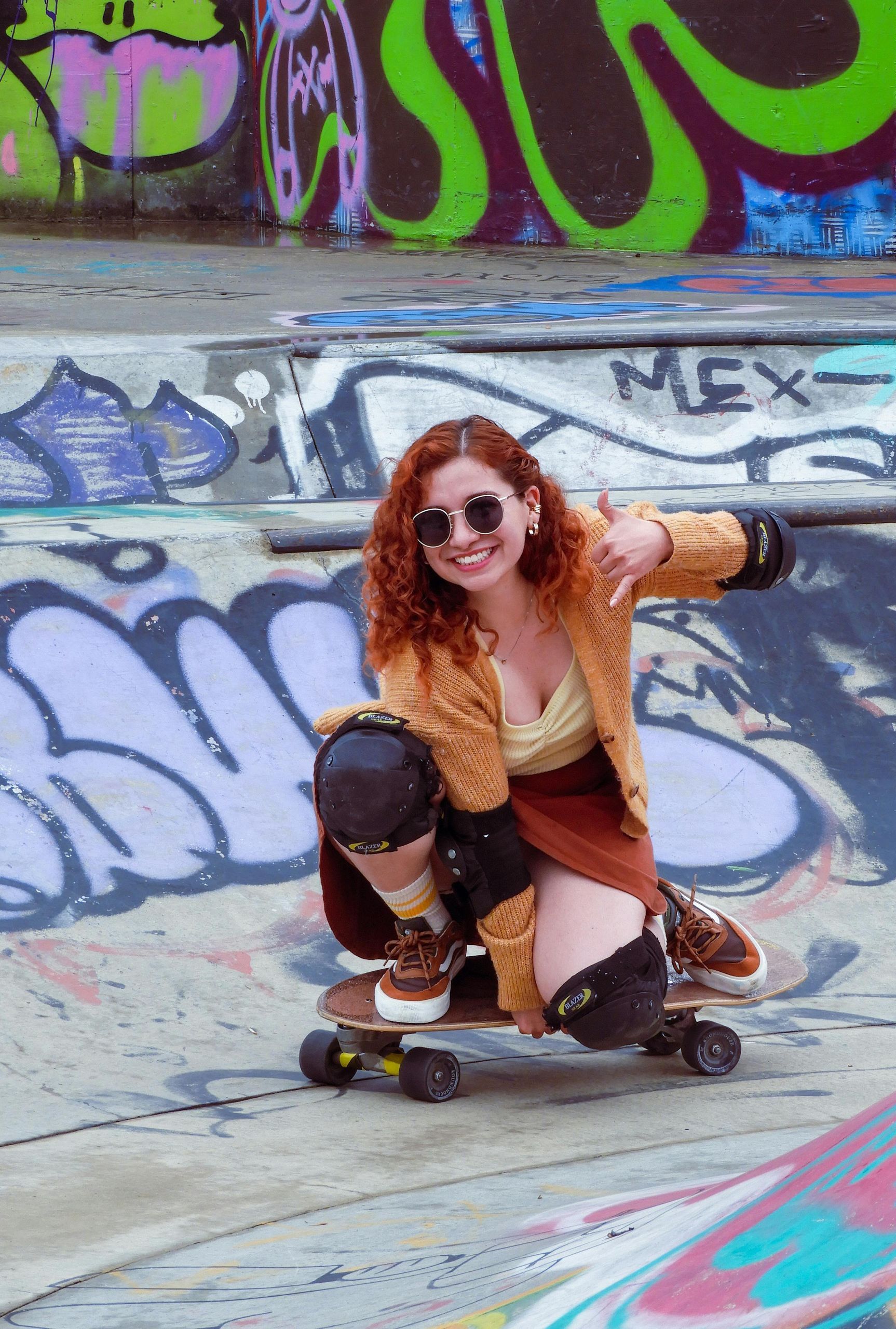 A woman is kneeling on a skateboard in front of a graffiti wall.
