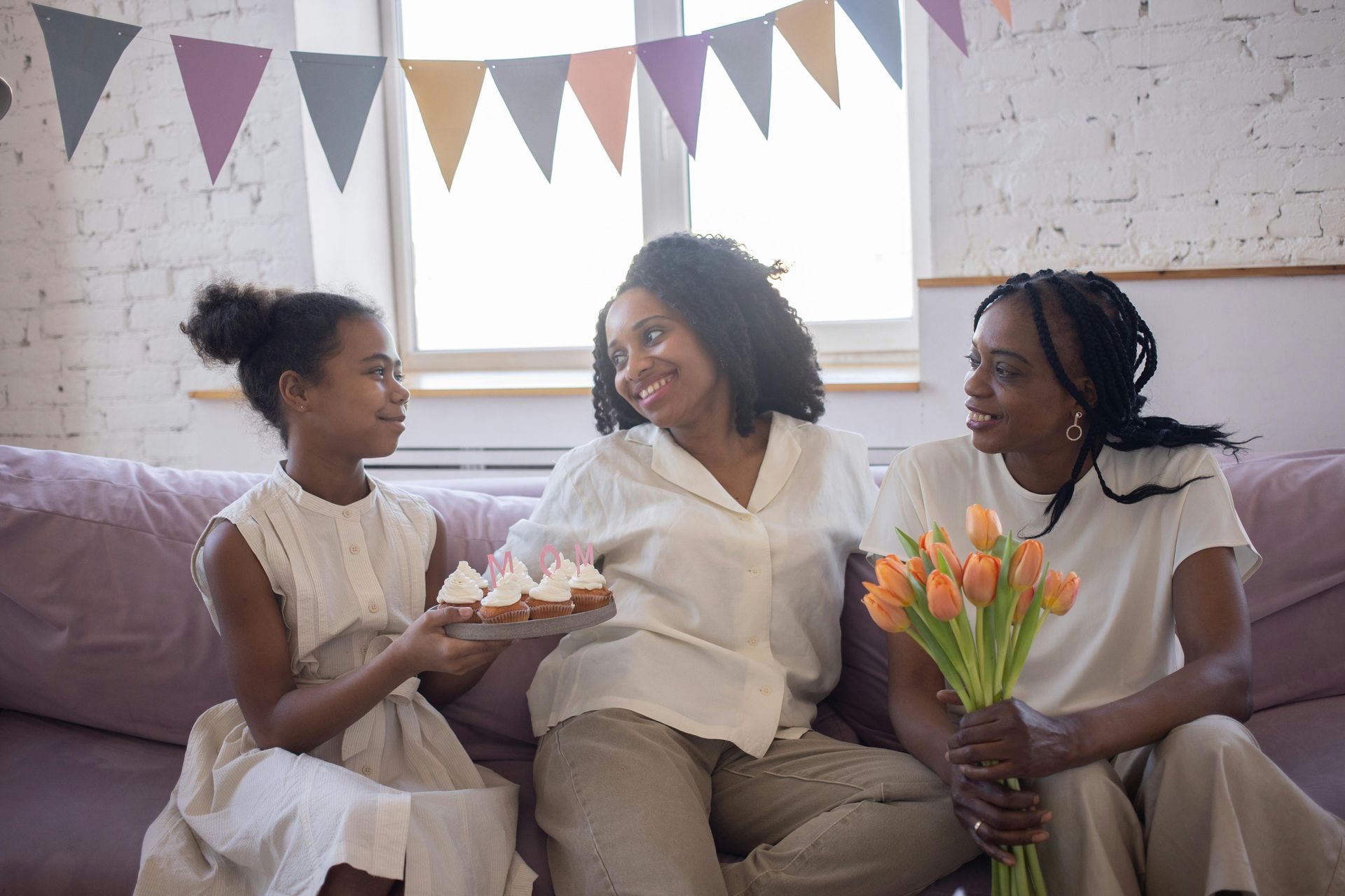 3 women sit on a couch together and talk and laugh.