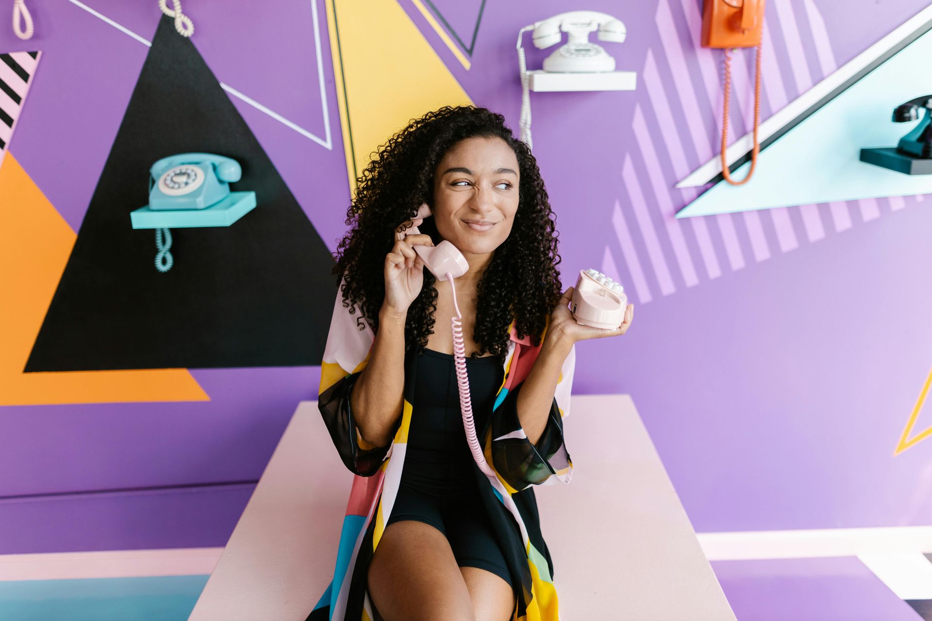 A woman is sitting on a table talking on a telephone.