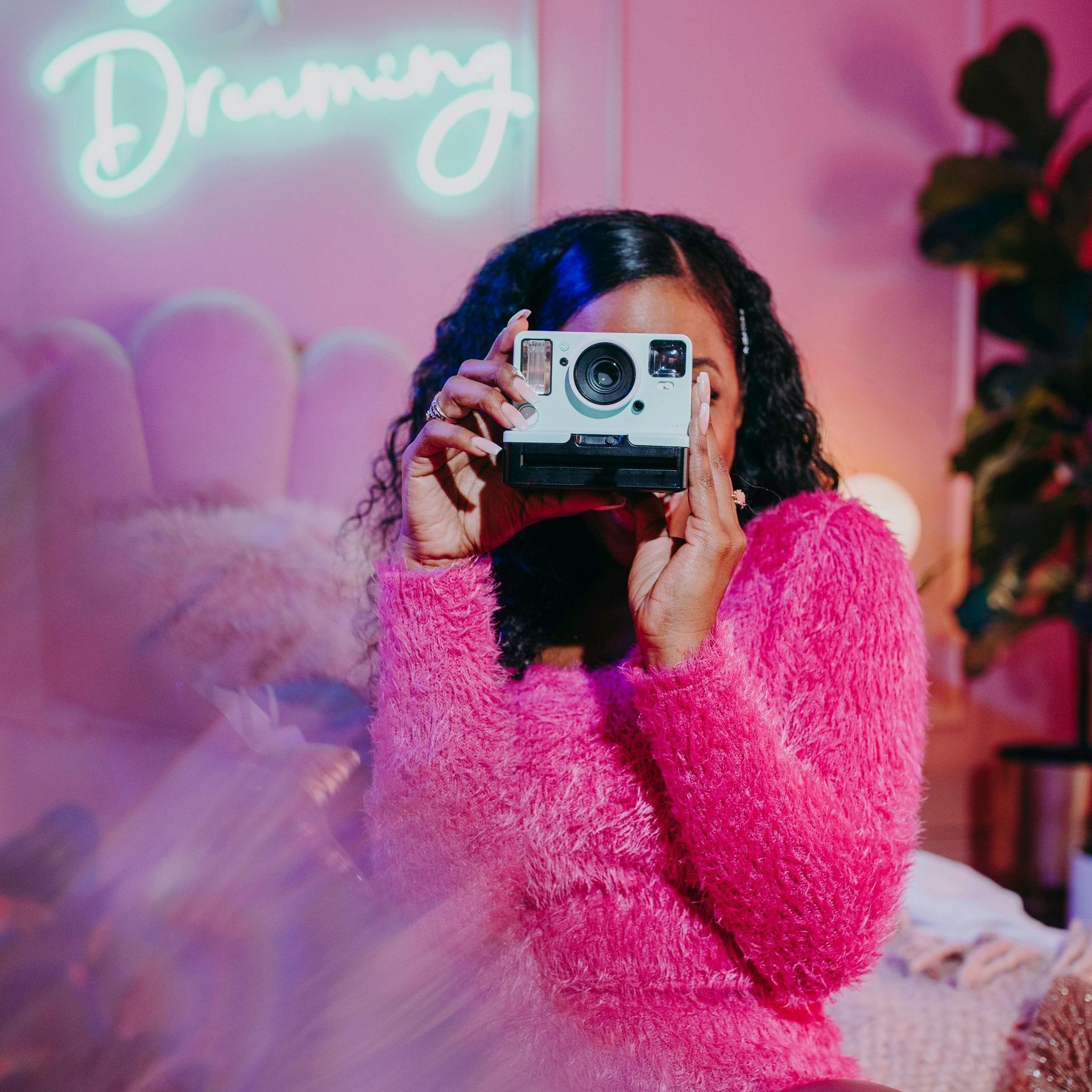 A woman in a pink sweater is holding a camera in front of her face.