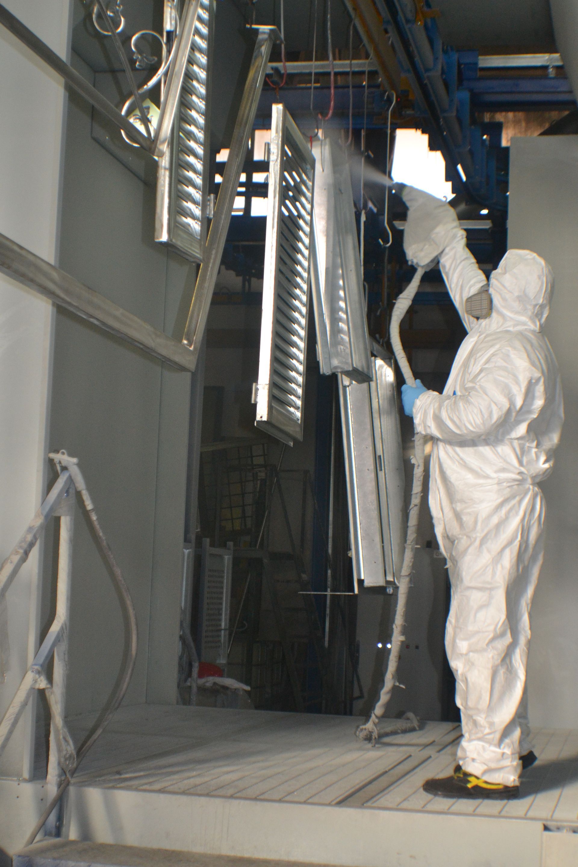 Un uomo con una tuta protettiva sta verniciando un pezzo di metallo in una fabbrica.
