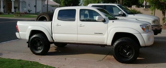 Two white trucks are parked in a driveway next to each other.