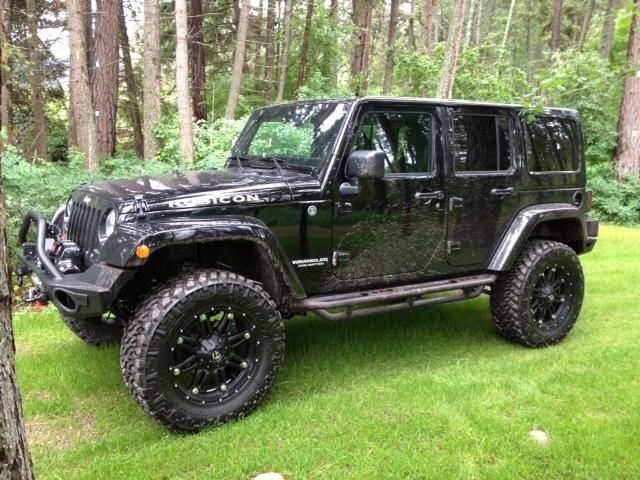 A black jeep is parked in the grass in front of a forest.