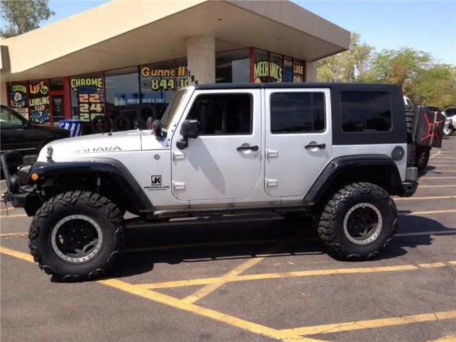 A silver jeep is parked in a parking lot in front of a gas station.