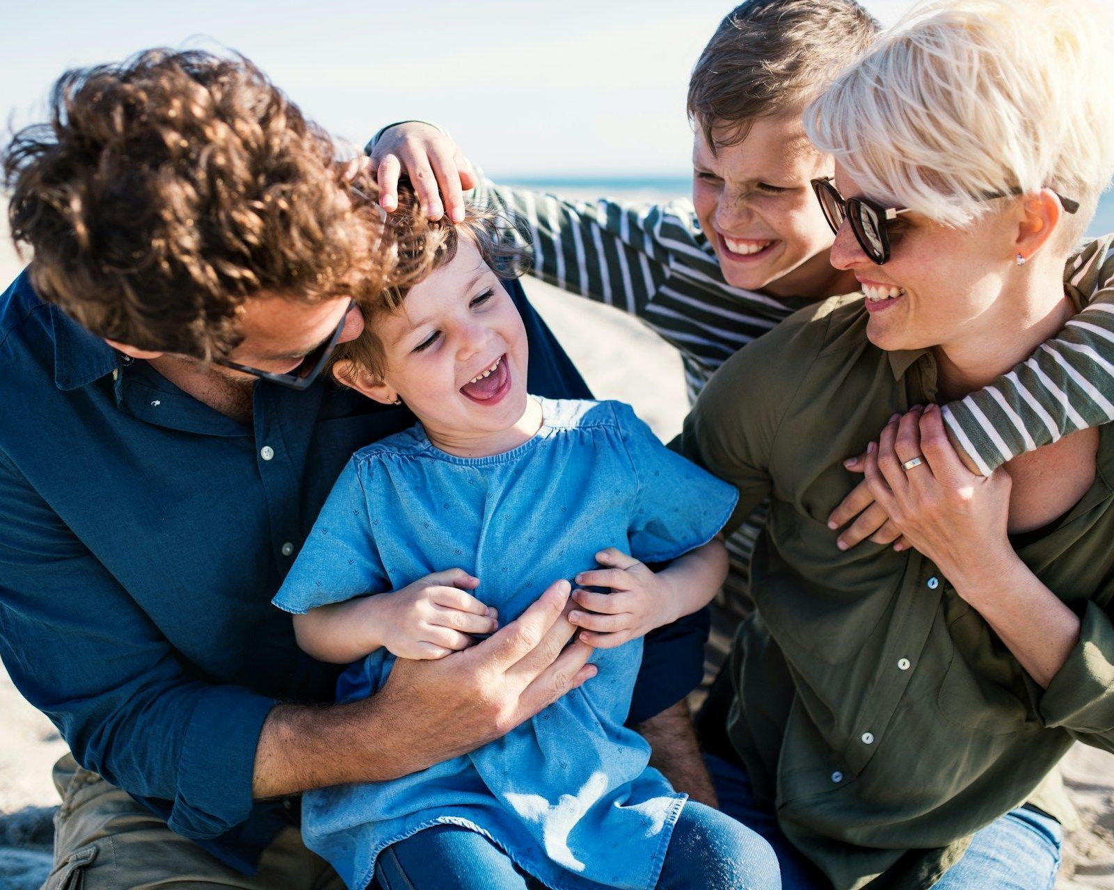 A family is sitting on the beach playing with each other.