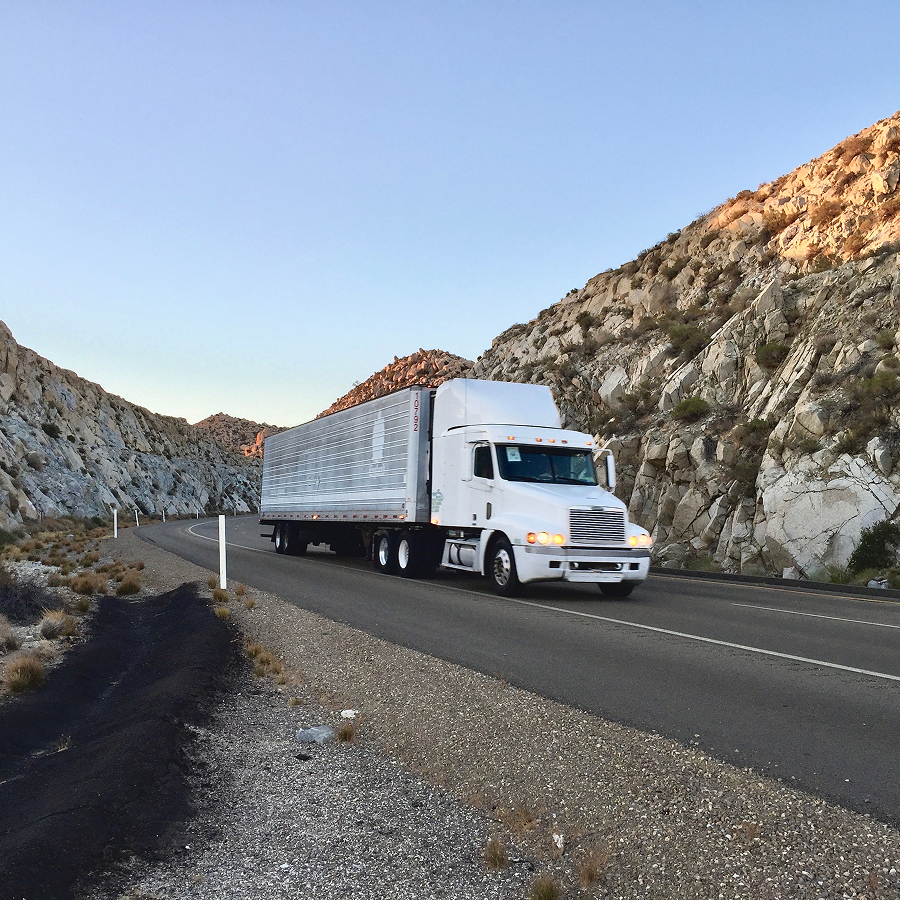 A white semi truck is driving down a mountain road