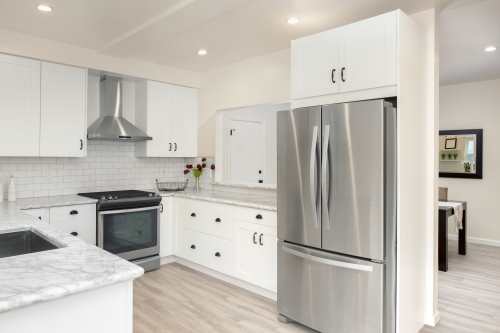 la cucina con mobili bianchi con top in marmo e un frigo