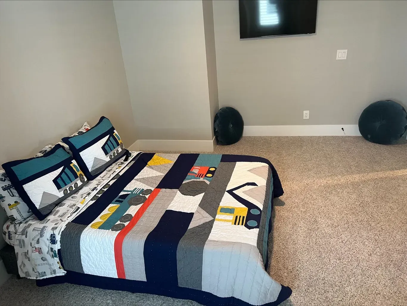 Bed with construction-themed bedding in a room with a TV and exercise balls.