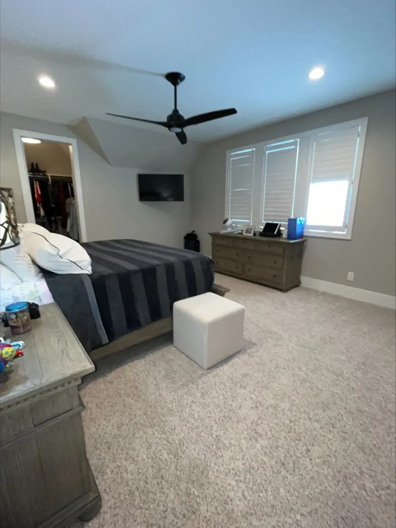 Bedroom with a bed, dresser, TV, and open closet door. Gray walls, light carpet, and a ceiling fan.