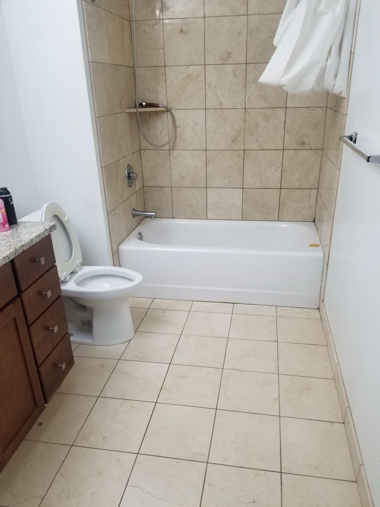 Bathroom with a white bathtub, toilet, and tan tile walls and floor. Brown vanity.