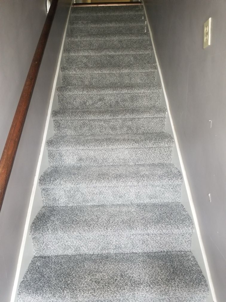 Gray carpeted staircase with white trim and a wooden handrail.