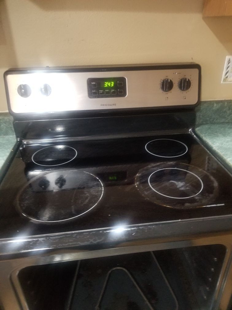 Black electric stove with four burners, controls, and oven. Silver control panel, black glass top.
