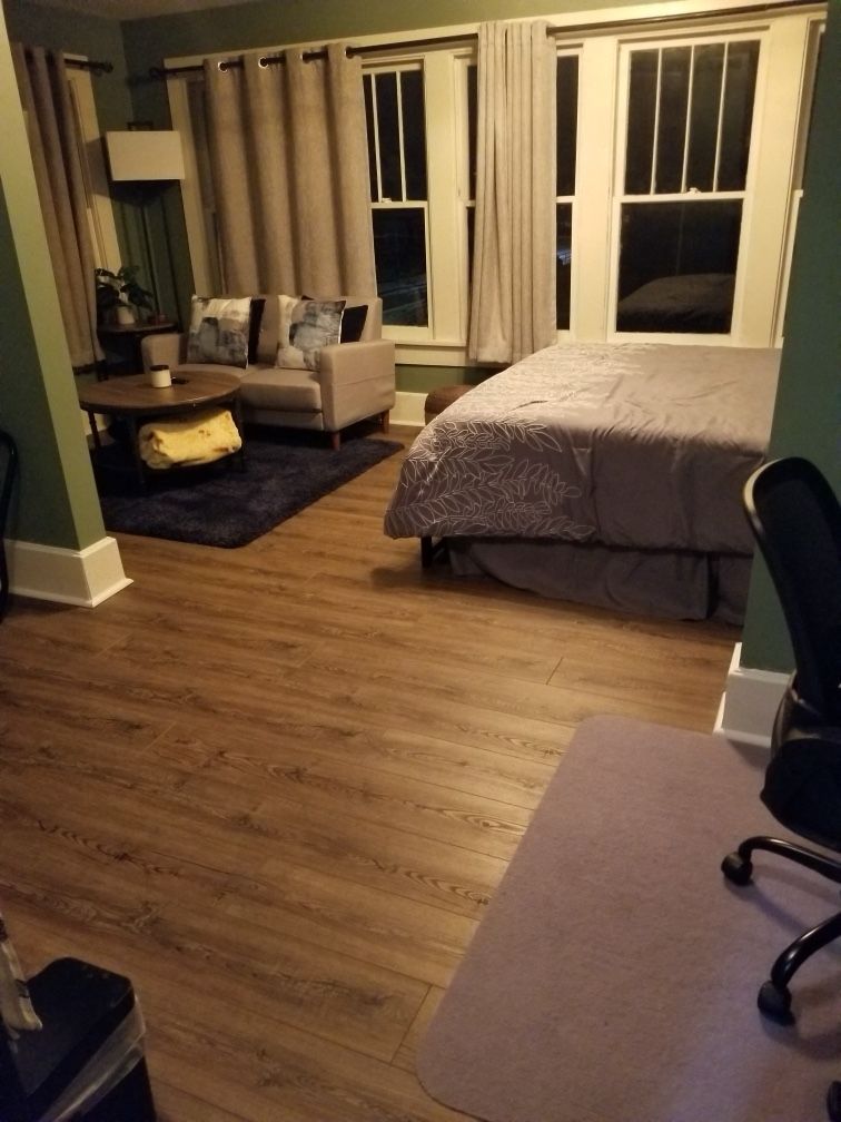 Bedroom with a bed, couch, coffee table, and windows. Brown floor, gray and white furniture, and dark green walls.