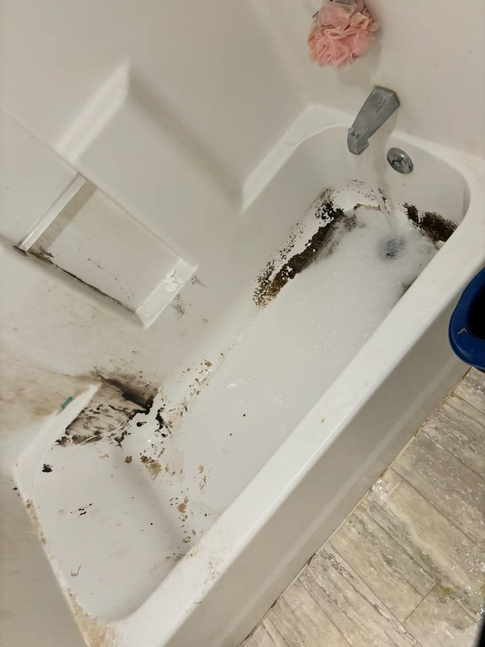 A dirty bathtub in a bathroom with foam coming out of it.