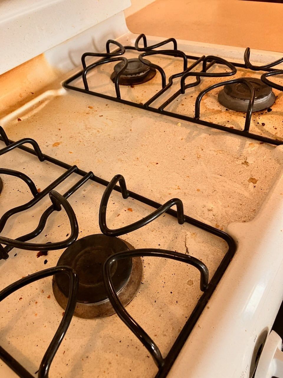 Dirty gas stovetop with black grates and burner tops, covered in a light-colored, stained surface.