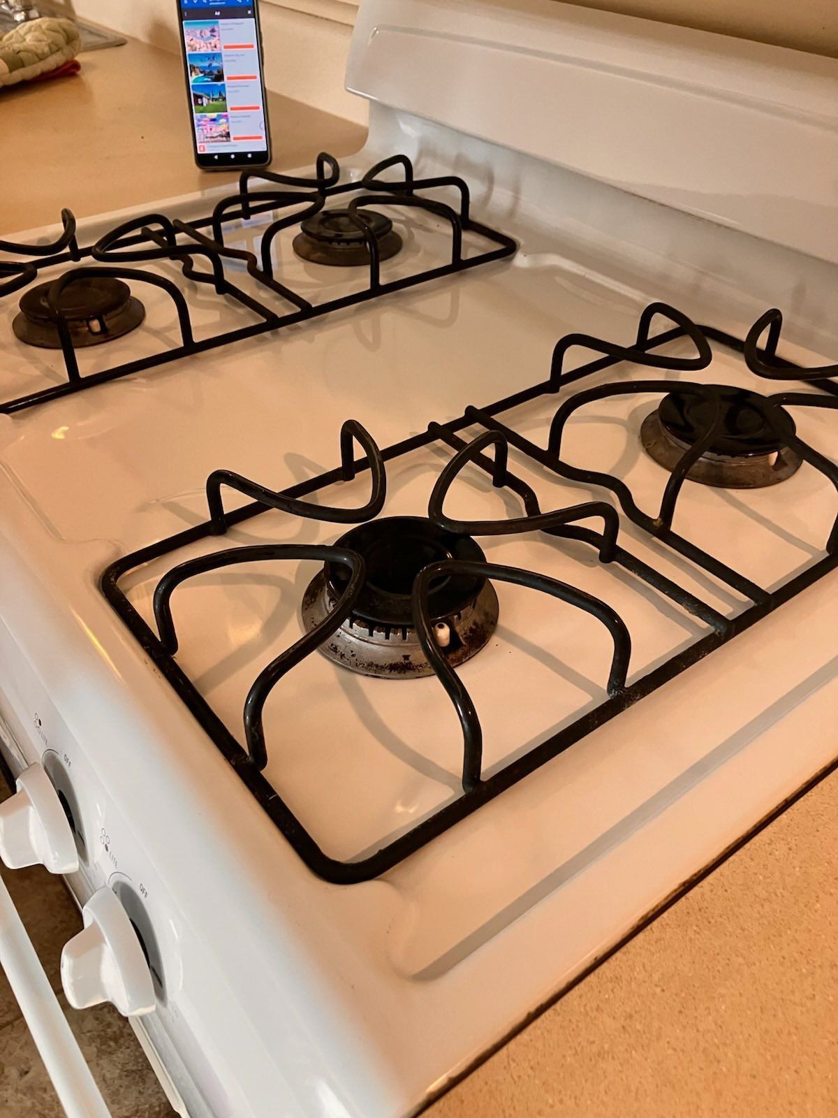 A white gas stove with three burners and a cell phone on the counter.