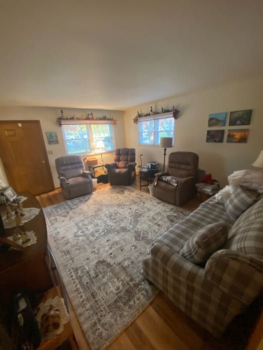 Living room with rug, recliner chairs, plaid couch, windows, and decorative wall art.