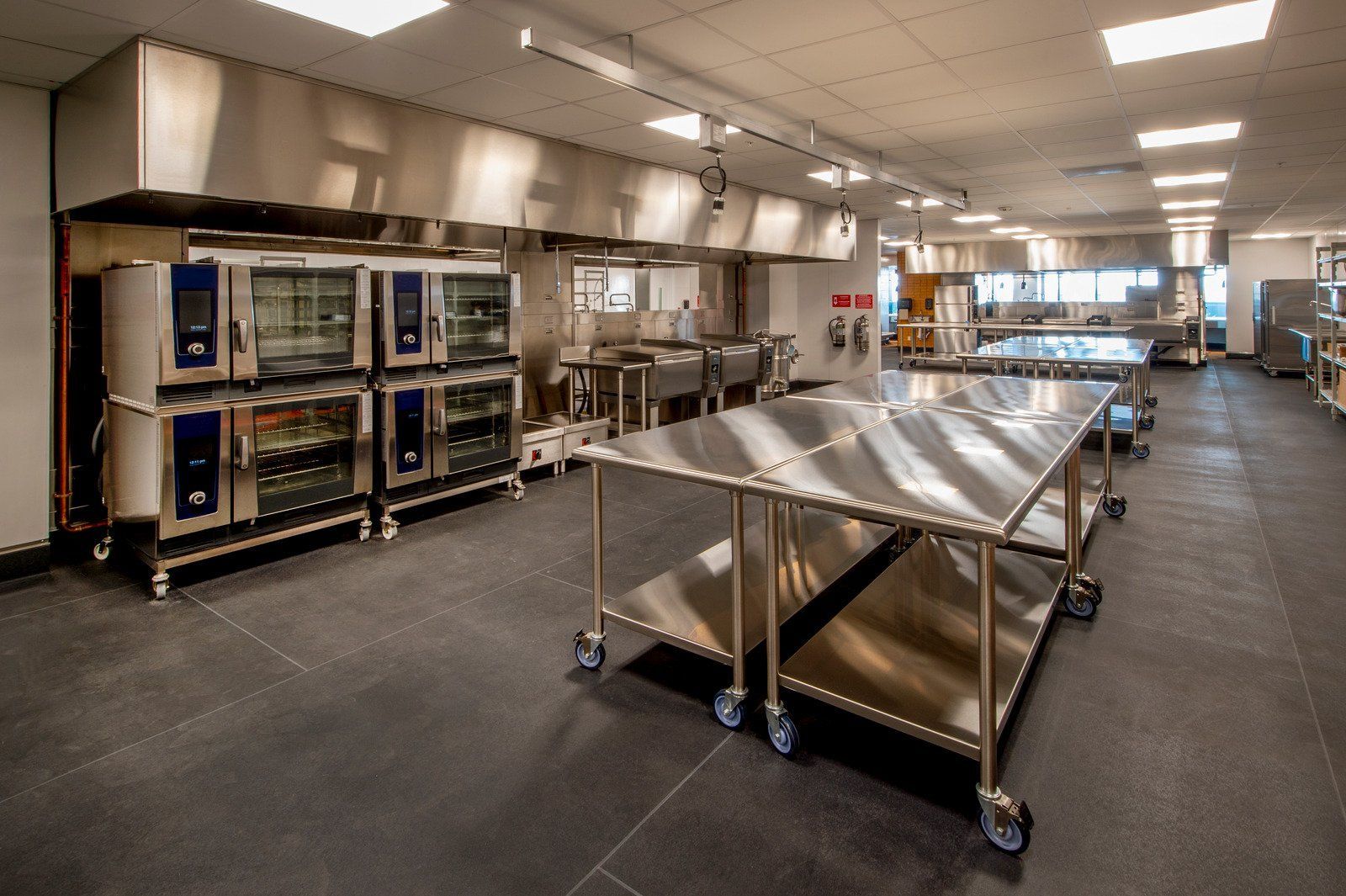 Commercial kitchen with stainless steel equipment and work tables.