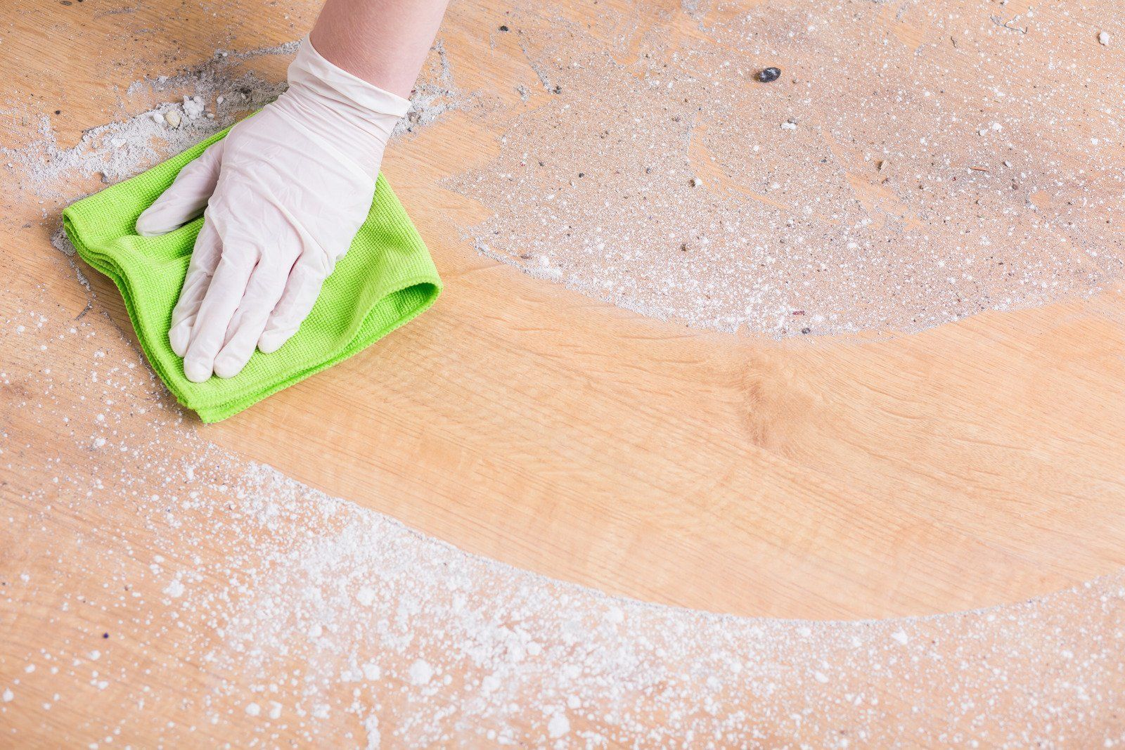 A person is cleaning a wooden floor with a green cloth.