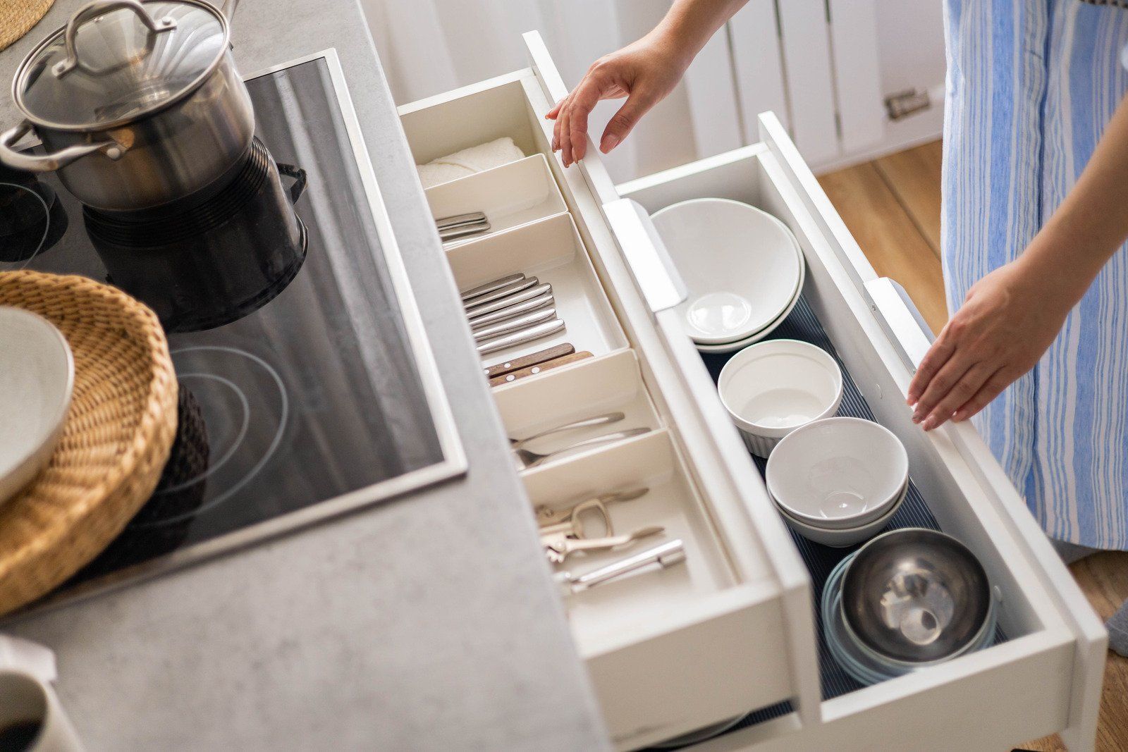A woman is opening a drawer in a kitchen filled with bowls and silverware.