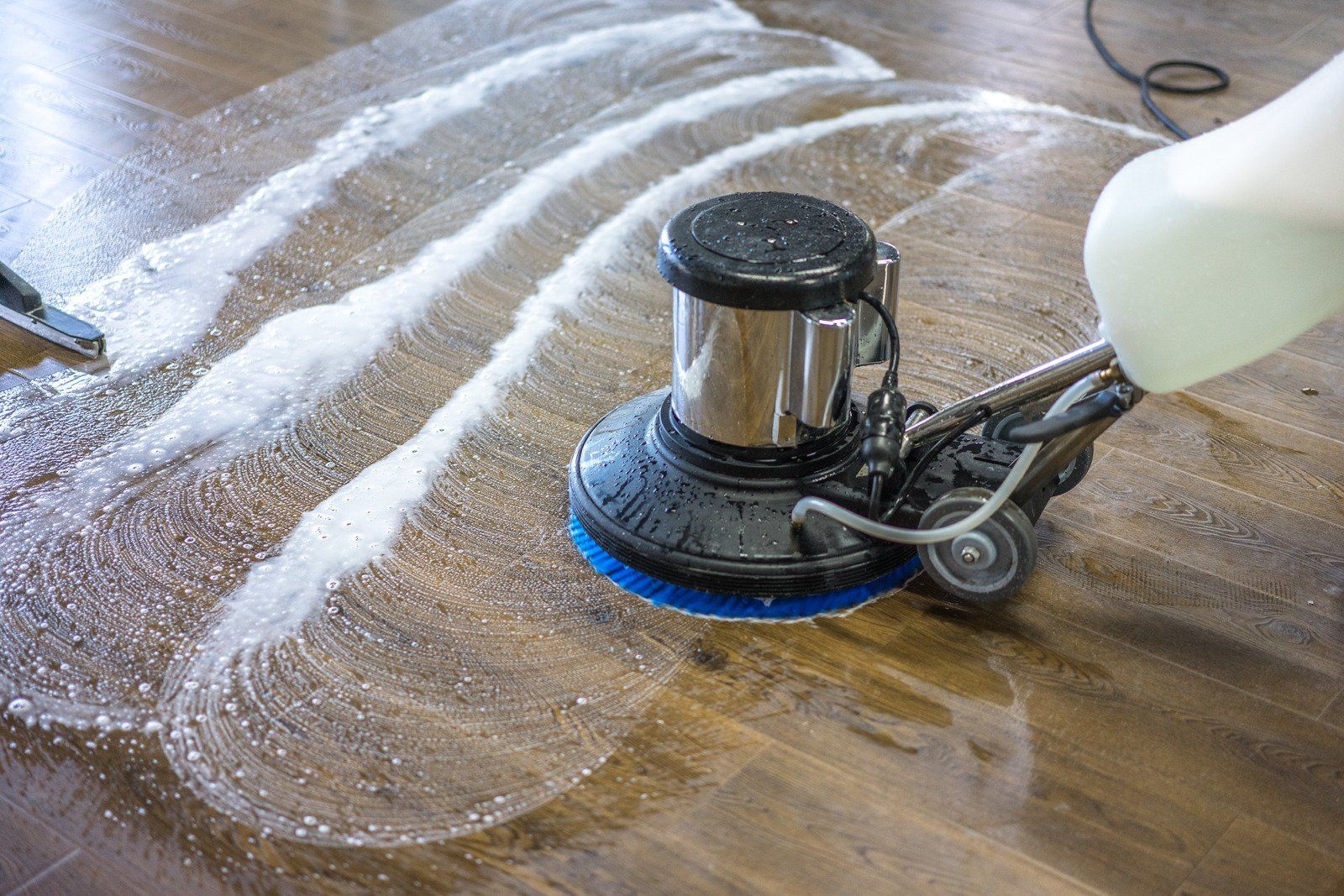 A person is cleaning a wooden floor with a machine.