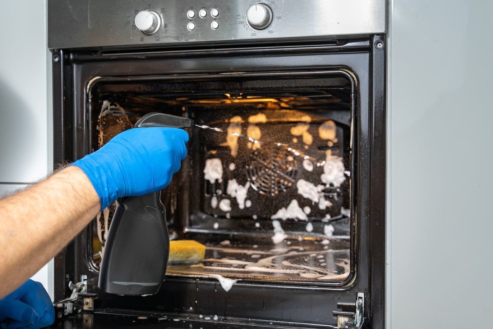 A person is cleaning an oven with a spray bottle.