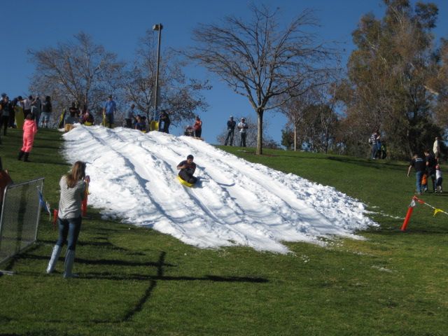 People are sledding down a snowy hill in a park