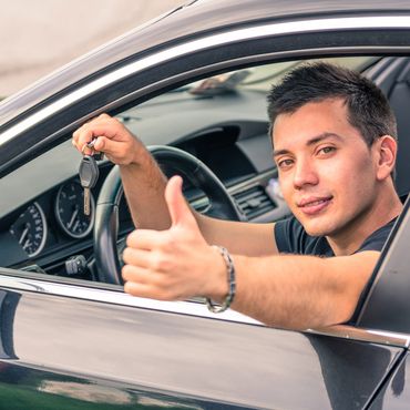 A young man sticking up his thumb as he holds the keys to his new car