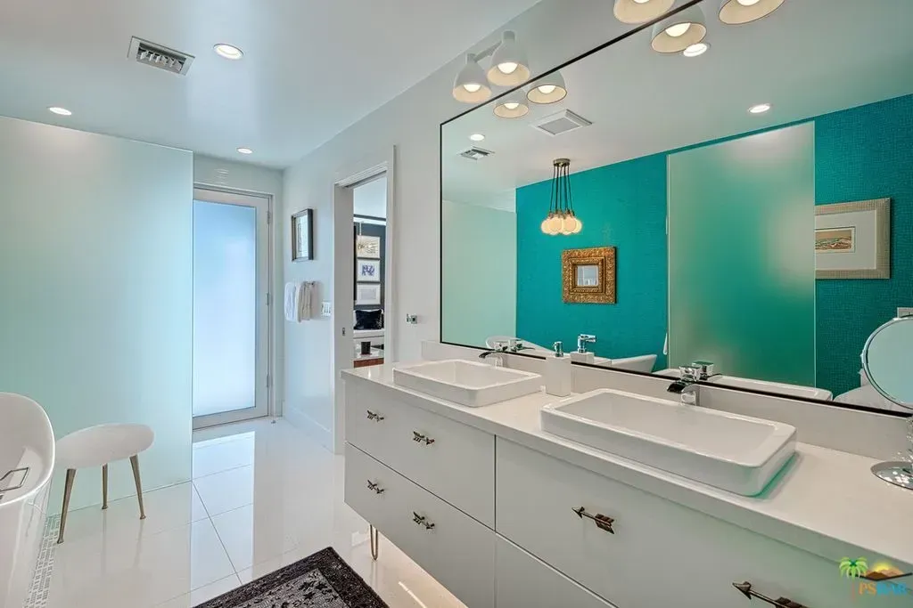 Bright modern bathroom with double vanity, large mirror, white tiles, and teal accent wall