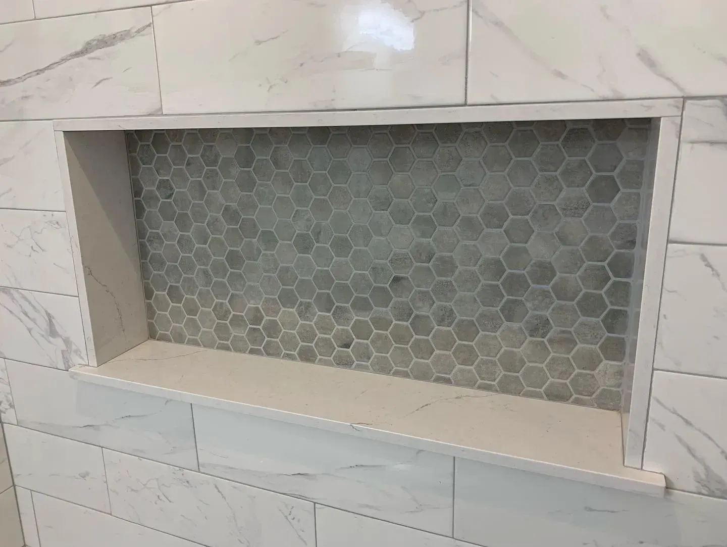 Recessed wall niche with gray hex tile backing and white marble-style surround