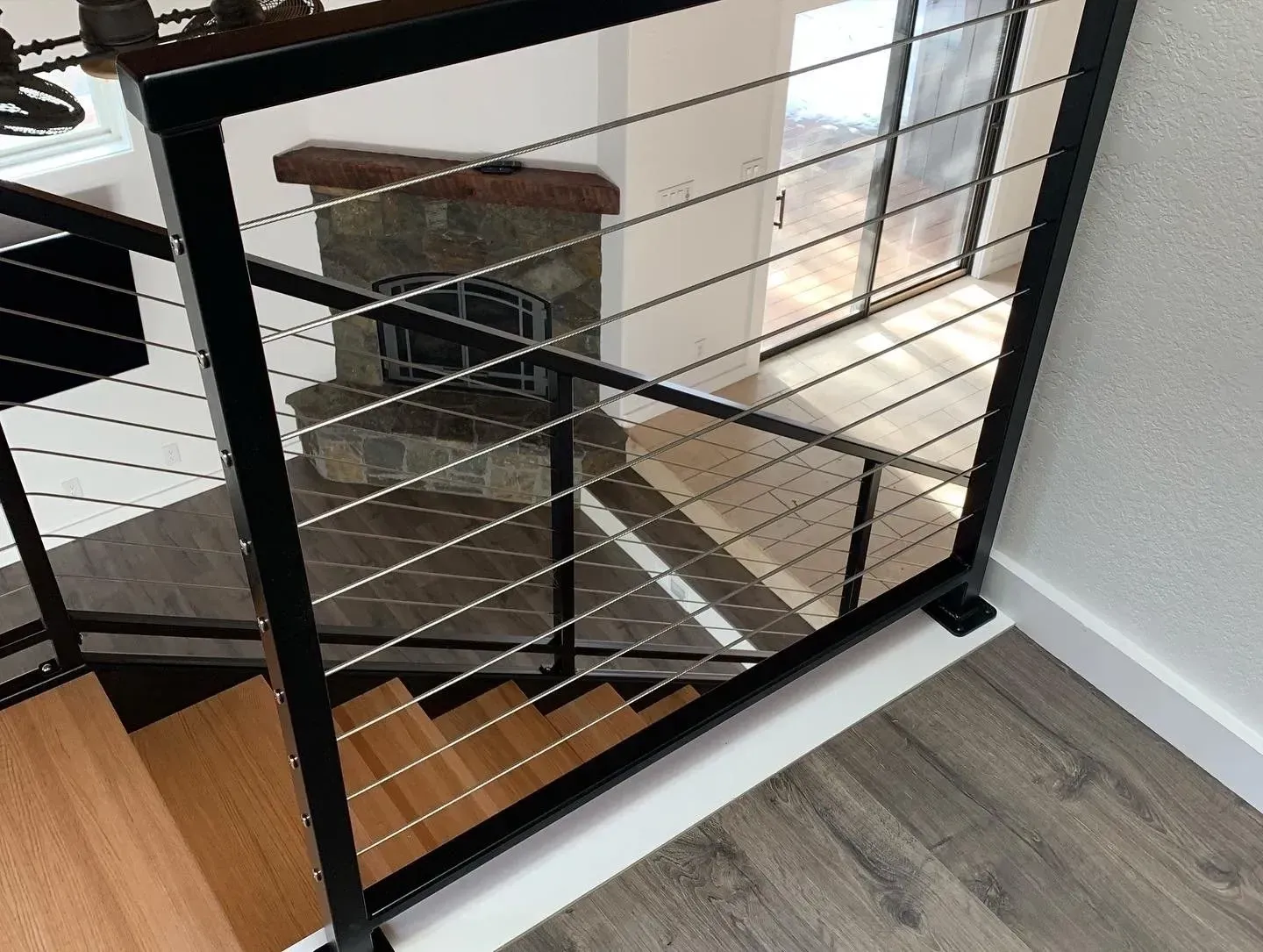 Black metal staircase railing overlooking a wooden stair landing and gray wood floor indoors