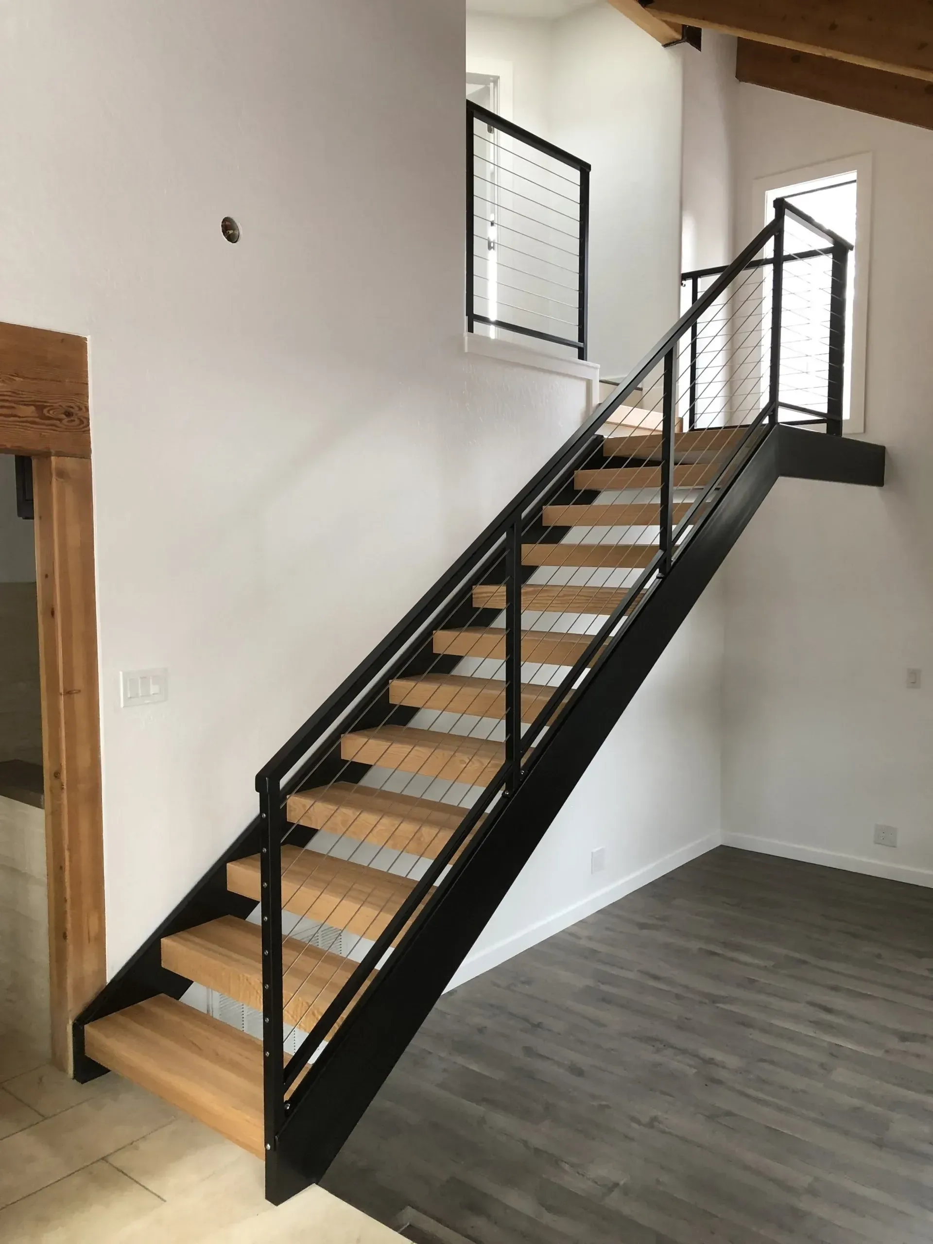 Modern indoor staircase with black railings and light wood steps in a white room