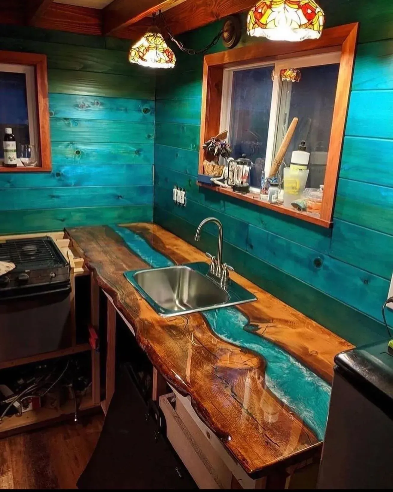 Rustic kitchen with turquoise wood walls, a wooden countertop, sink, and colorful hanging lights.