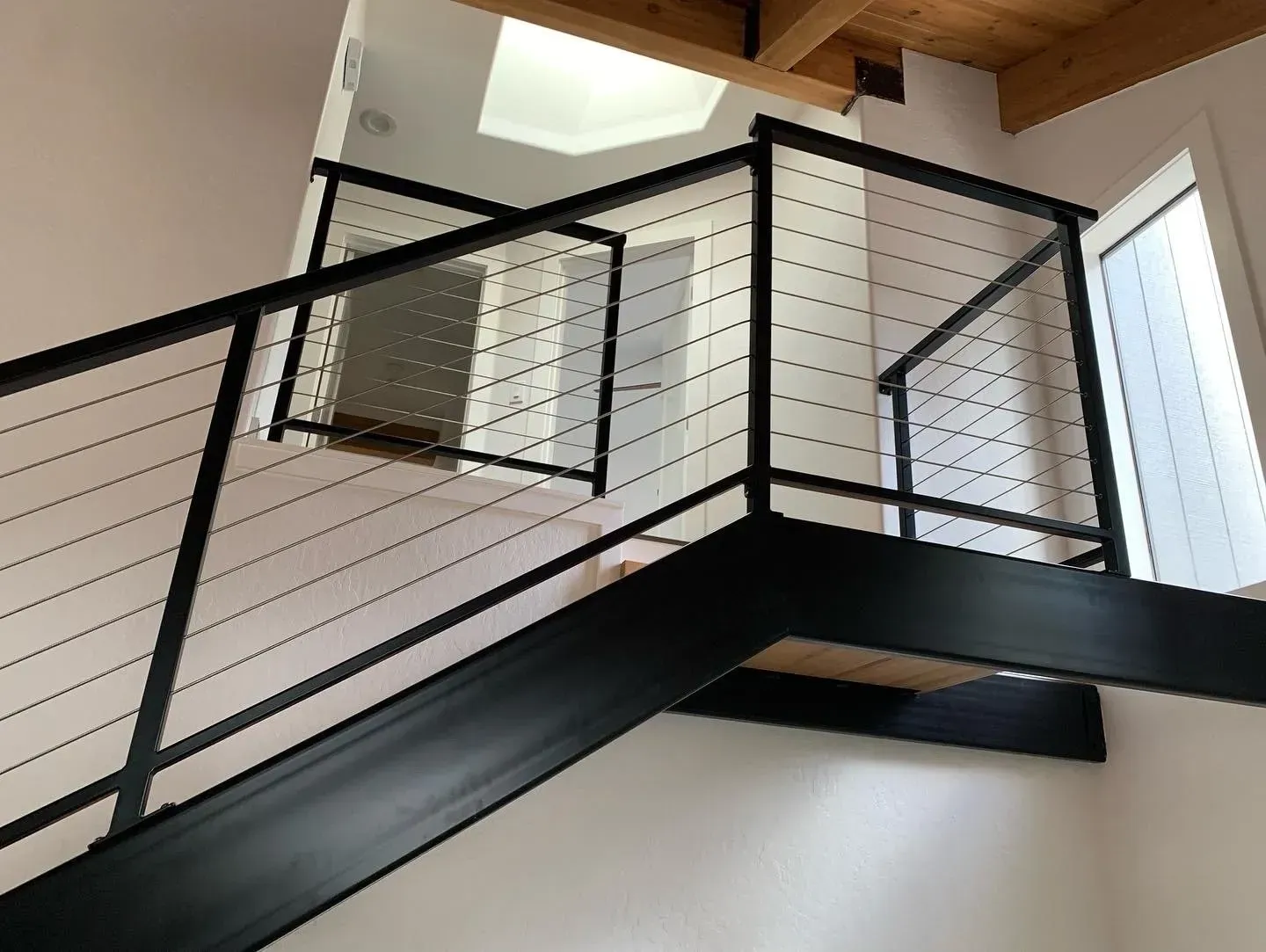Modern indoor staircase with black metal railing and white walls under a skylight