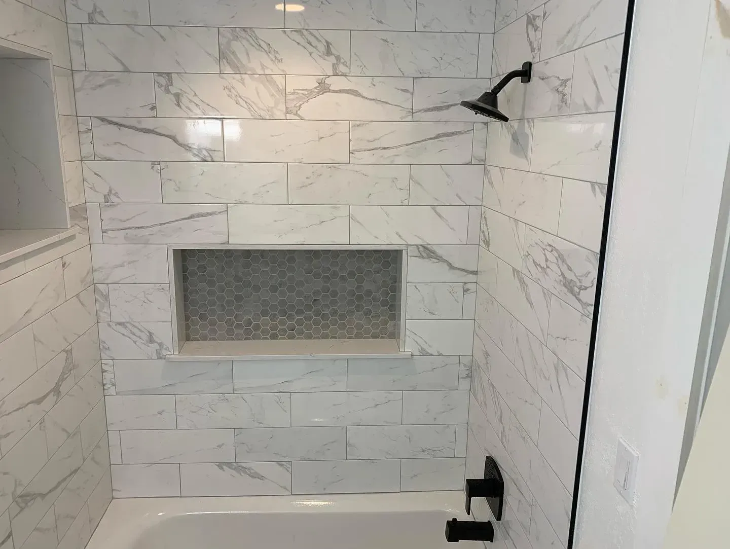 Marble-tiled shower with a recessed niche and black shower fixtures