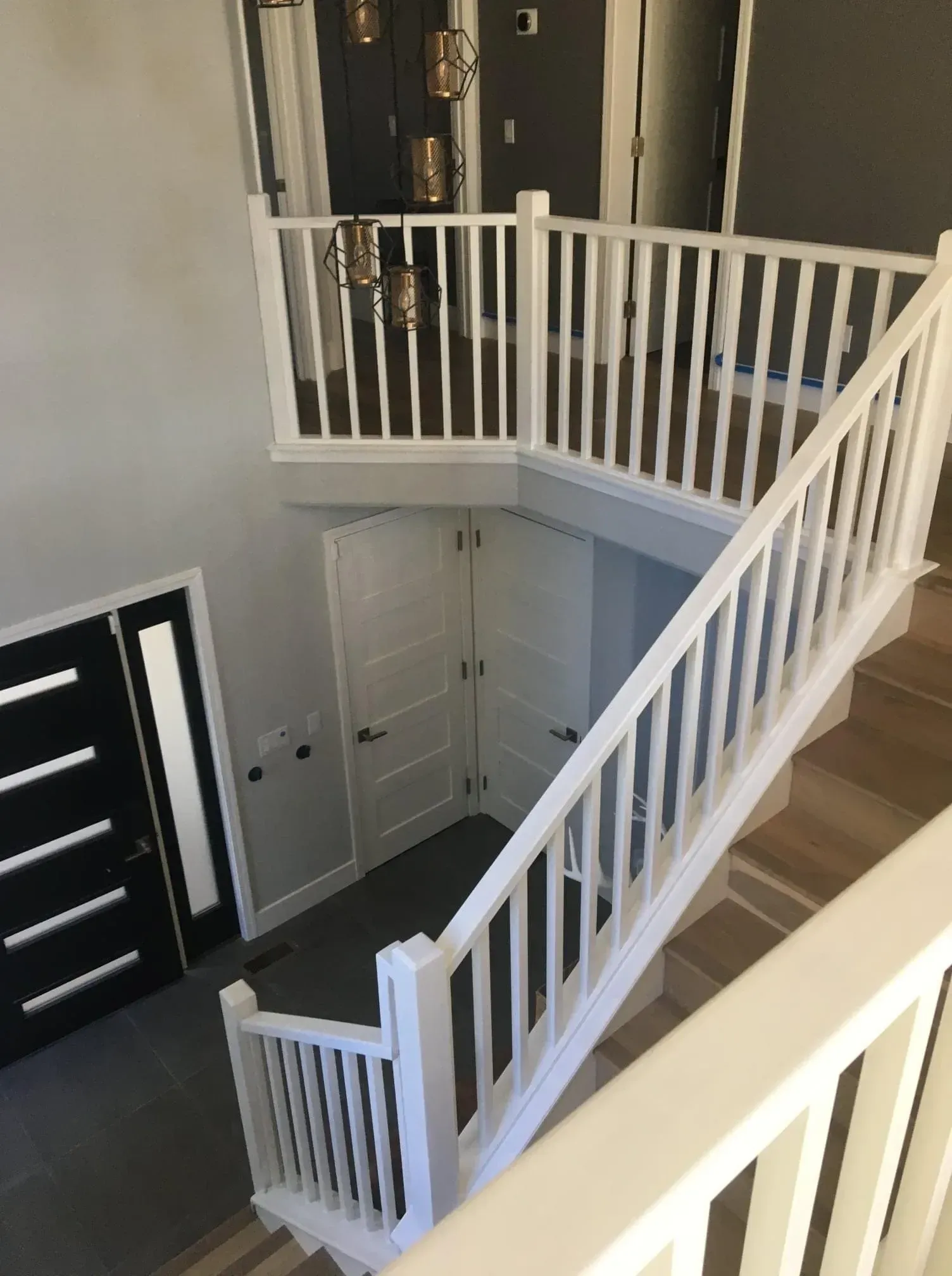 Interior staircase with white railings, dark front door, and light wood flooring in a two-story entryway